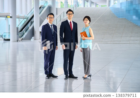 三位日本商務人士面帶微笑，充滿自信，站在一棟辦公大樓寬敞的大廳裡。 138379711