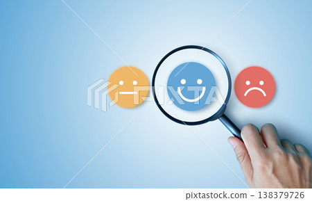 Hand holding magnifying glass focusing on happy smile face over neutral and sad icons on blue background. Concept of customer satisfaction survey, finding positive feedback and excellent service. Hand holding magnifying glass focusing on happy smile face over neutral and sad icons on blue background. Concept of customer satisfaction survey, finding positive feedback and excellent service. 138379726