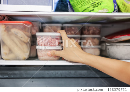 Close up of woman hand taking clear plastic food containers with raw minced meat from the freezer. Organizing refrigerator, daily food preparation, meal prep, household routine and kitchen storage. Close up of woman hand taking clear plastic food containers with raw minced meat from the freezer. Organizing refrigerator, daily food preparation, meal prep, household routine and kitchen storage. 138379751