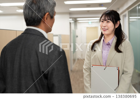 一名男性和一名女性辦公室職員正在走廊上交談，討論與工作有關的事。 138380695