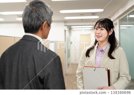 一名男性和一名女性辦公室職員正在走廊上交談，討論與工作有關的事。 138380696