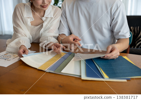A young couple holds wallpaper samples in their hands as they discuss the issue. 138381717