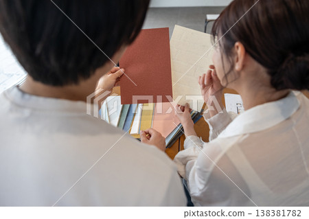 A young couple, seen from behind, discussing wallpaper samples. 138381782