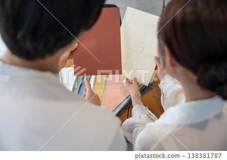一對年輕夫婦正在討論壁紙樣品，鏡頭對準了他們的背影。 138381787