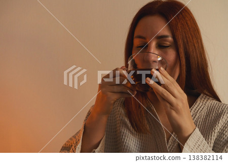 Woman with red hair enjoying warm beverage in a cozy atmosphere, practicing self-care and unwinding at home, relaxing drinking hot tea for wellness. 138382114