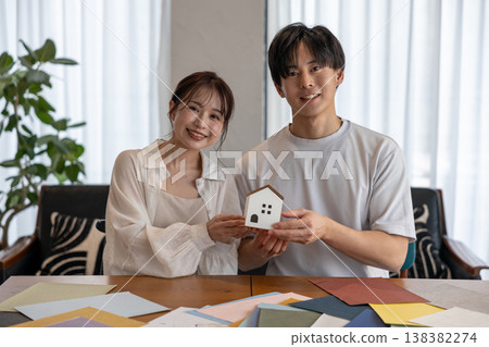 A young couple smiling while holding a house-shaped ornament. A young couple smiling while holding a house-shaped ornament. 138382274