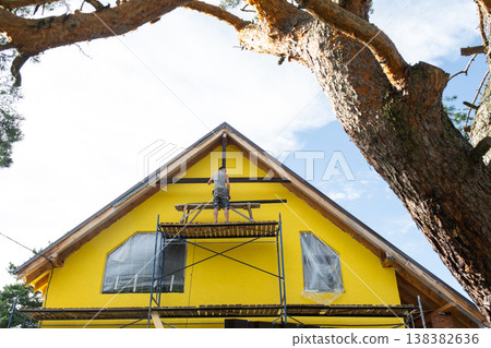 Wide view of bright yellow home with scaffolding and gable work in progress, sunny construction scene, home improvement ongoing. Wide view of bright yellow home with scaffolding and gable work in progress, sunny construction scene, home improvement ongoing. 138382636