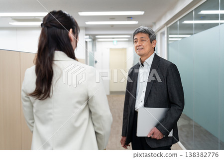 一名男性和一名女性辦公室職員正在走廊上交談，討論與工作有關的事。 138382776