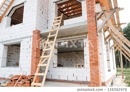 Close-up of brick and aerated concrete house, workers assembling roof frame, clearly visible rafter lags, European construction method. 138382978