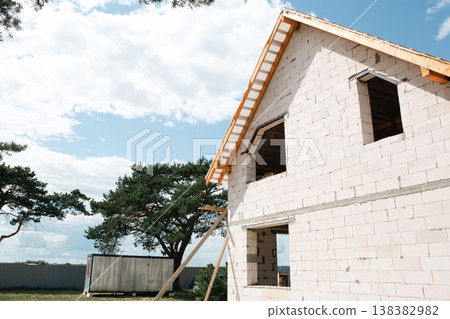 Perspective view of new house during roof system assembly, trusses and lags form modern Eurostyle silhouette, brick and white block wall. Perspective view of new house during roof system assembly, trusses and lags form modern Eurostyle silhouette, brick and white block wall. 138382982