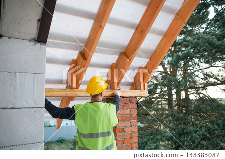 Construction site master checks evenness of rafters for insulated roof, modern build in progress, timber lag placement visualized. Construction site master checks evenness of rafters for insulated roof, modern build in progress, timber lag placement visualized. 138383087