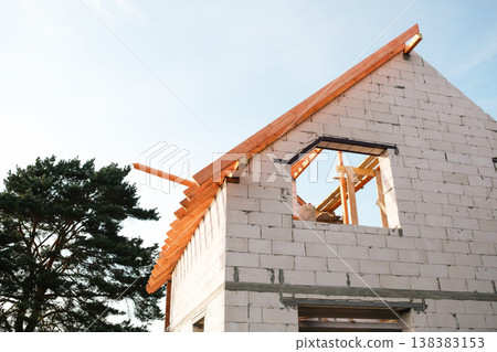 Modern white block house at step of affixing roof rafters, timber lag layout visible, credit used for home-building, financial security by insurance. Modern white block house at step of affixing roof rafters, timber lag layout visible, credit used for home-building, financial security by insurance. 138383153