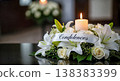 condolences ribbon text funeral white lilies roses flower bouquet glowing candle dark reflective table background mourning sorrow grief sympathy remembrance copy space obituary card 138383399