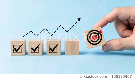 Hand placing wooden cube with target icon near blocks showing checkmarks under rising financial growth chart arrow representing business success goal achievement planning 138383407