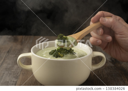 用湯匙舀起熱氣騰騰的青花菜湯。 用湯匙舀起熱氣騰騰的青花菜湯。 138384026