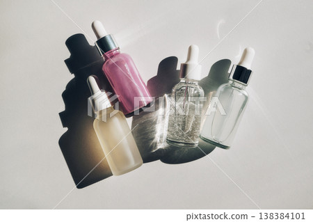 Skincare liquids and oils in glass dropper bottles on white surface, creating interesting shadows Skincare liquids and oils in glass dropper bottles on white surface, creating interesting shadows 138384101