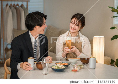 一對年輕的亞洲夫婦（啤酒，罐裝啤酒）在家裡的餐桌上吃喝。 138384419