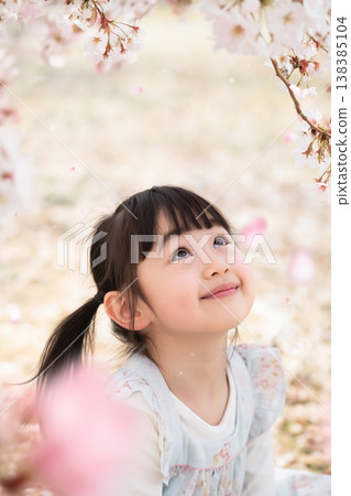 A girl smiles as she looks up at the cherry blossoms and the petals flutter down. 138385104