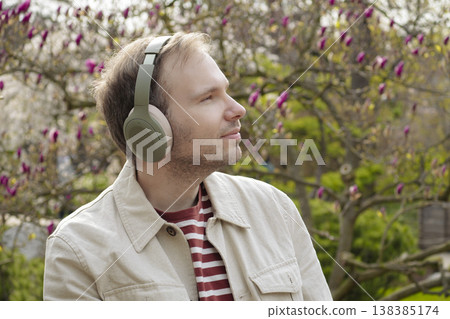 A smiling man with headphones relaxes in nature among blooming magnolias in a Japanese park, enjoying a digital detox. A smiling man with headphones relaxes in nature among blooming magnolias in a Japanese park, enjoying a digital detox. 138385174