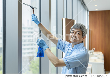 A senior male cleaning staff member smiles and looks directly at the camera. 138385303