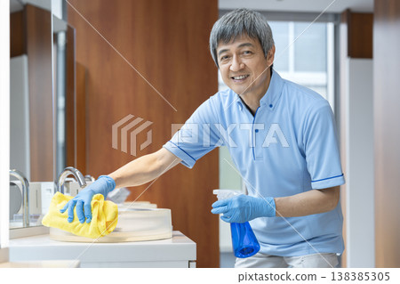 A senior male cleaning staff member smiles and looks directly at the camera. A senior male cleaning staff member smiles and looks directly at the camera. 138385305