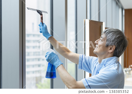 一名資深男性清潔工正在擦拭窗戶。 一名資深男性清潔工正在擦拭窗戶。 138385352