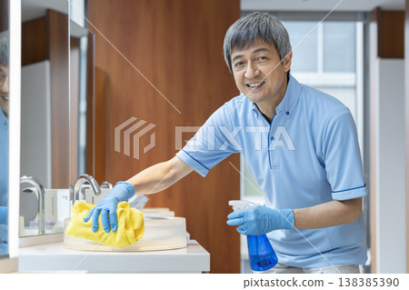A senior male cleaning staff member smiles and looks directly at the camera. A senior male cleaning staff member smiles and looks directly at the camera. 138385390