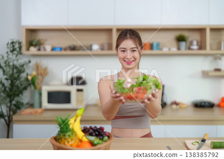 Smiling woman presenting fresh salad in home kitchen Smiling woman presenting fresh salad in home kitchen 138385792
