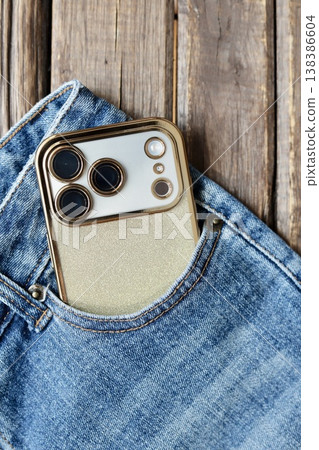 A triple-camera smartphone with a gold back case, placed in a denim pocket. A triple-camera smartphone with a gold back case, placed in a denim pocket. 138386604
