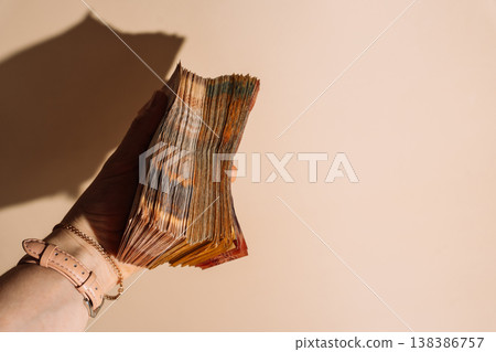 Hand holding a large bundle of Kazakhstani tenge banknotes on beige background, cash savings concept Hand holding a large bundle of Kazakhstani tenge banknotes on beige background, cash savings concept 138386757