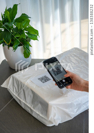 Person scanning QR code on parcel with smartphone camera for delivery tracking at home. Contactless technology mobile app and digital service concept. 138388232