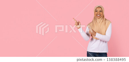 Young black Muslim woman in hijab pointing sideways at copy space 138388495
