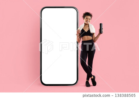 Sporty Black woman with towel and water bottle standing beside smartphone mockup Sporty Black woman with towel and water bottle standing beside smartphone mockup 138388505