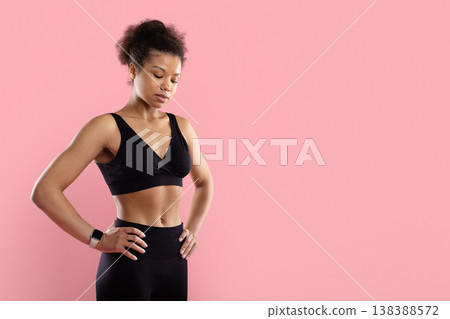 Focused Black sportswoman standing with hands on hips looking down 138388572