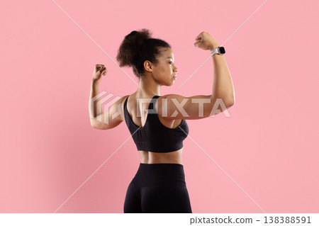 Strong black woman flexing back muscles in sportswear on pink studio background Strong black woman flexing back muscles in sportswear on pink studio background 138388591