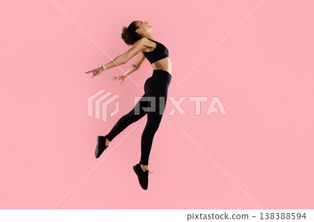 Athletic black woman jumping backward with arms open on pink studio background Athletic black woman jumping backward with arms open on pink studio background 138388594