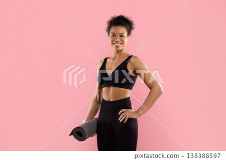 Smiling athletic black woman holding yoga mat on pink studio background Smiling athletic black woman holding yoga mat on pink studio background 138388597