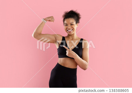Cheerful Black sportswoman flexing one bicep and pointing at her muscle Cheerful Black sportswoman flexing one bicep and pointing at her muscle 138388605