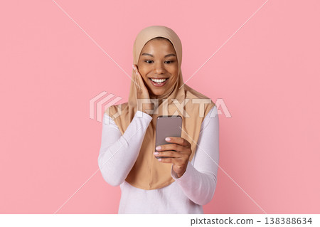 Young black Muslim woman in hijab reacting with surprise while reading smartphone 138388634