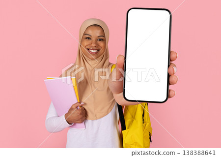 Young black Muslim woman student in hijab holding large blank smartphone screen Young black Muslim woman student in hijab holding large blank smartphone screen 138388641