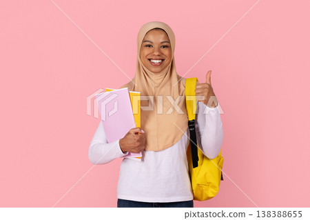 Black female student in hijab with backpack and books giving thumbs up 138388655
