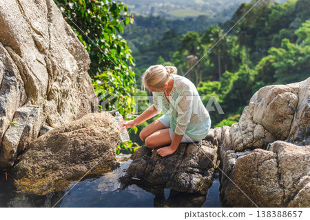 Woman collecting water from natural rock pool in tropical jungle, travel and eco lifestyle concept on Koh Samui island 138388657