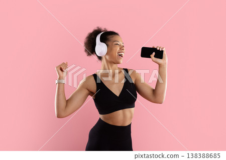 Energetic black woman with headphones holding smartphone like microphone 138388685