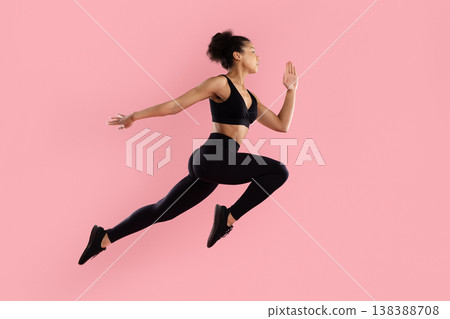 Athletic black woman performing dynamic running jump in sportswear on pink background 138388708