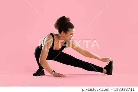 Fit black woman stretching leg in side lunge position on pink background Fit black woman stretching leg in side lunge position on pink background 138388711