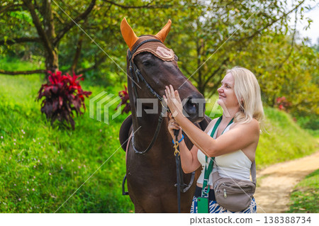 Young woman smiling while petting horse in tropical garden, emotional bond with animal during outdoor leisure activity 138388734