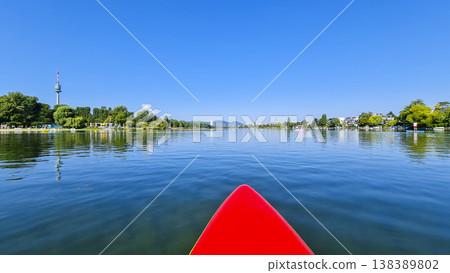 First-person view from a red stand-up paddleboard on a calm river with a city skyline. Summer water sport, mental vitality 138389802