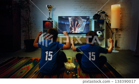 Two boys watching basketball game on TV at home celebrating victory together. 138390017