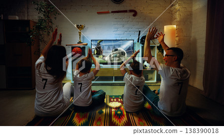 Family reacting to football save on TV at home clapping and raising hands together. 138390018