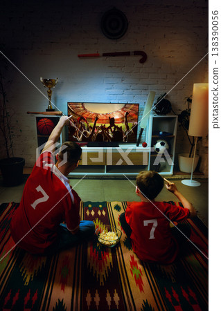 Father and son watching football match on TV at home pointing at screen together. 138390056